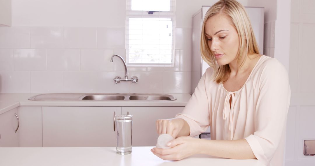 Woman Taking Medication with Glass of Water in Bright Kitchen - Free Images, Stock Photos and Pictures on Pikwizard.com