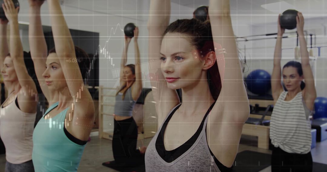 Group Fitness Class Holding Kettlebells Overhead in Gym Setting