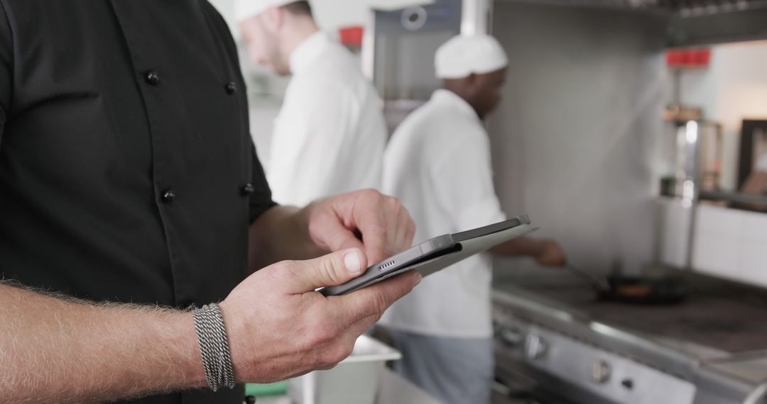 Chef using tablet in professional kitchen with cooking staff in background - Free Images, Stock Photos and Pictures on Pikwizard.com