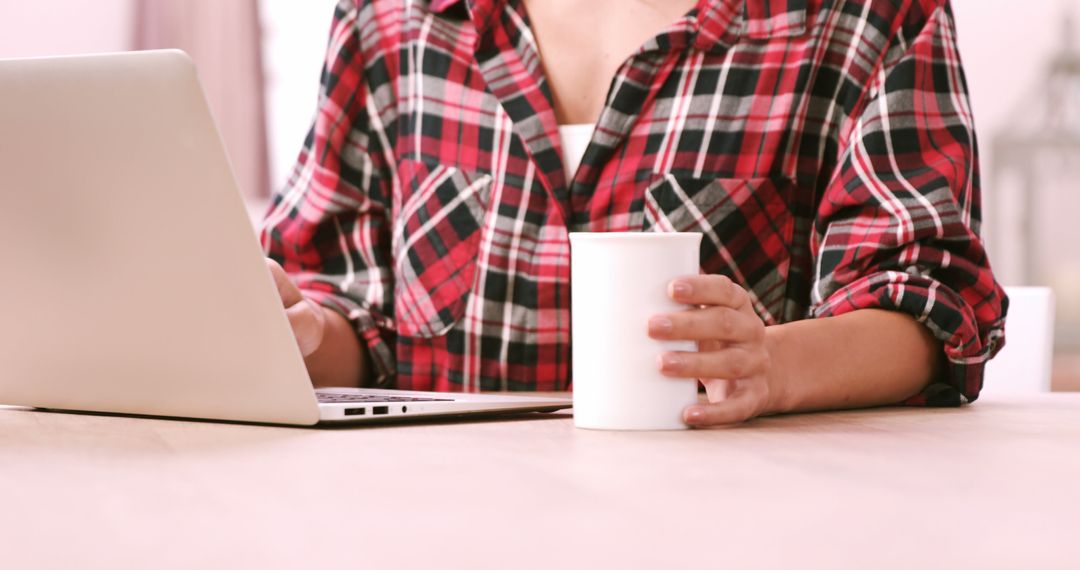 Woman Wearing Plaid Shirt Using Laptop and Holding Cup of Coffee - Free Images, Stock Photos and Pictures on Pikwizard.com