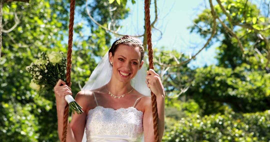 Happy bride sitting on a swing looking at camera on her wedding day - Free Images, Stock Photos and Pictures on Pikwizard.com