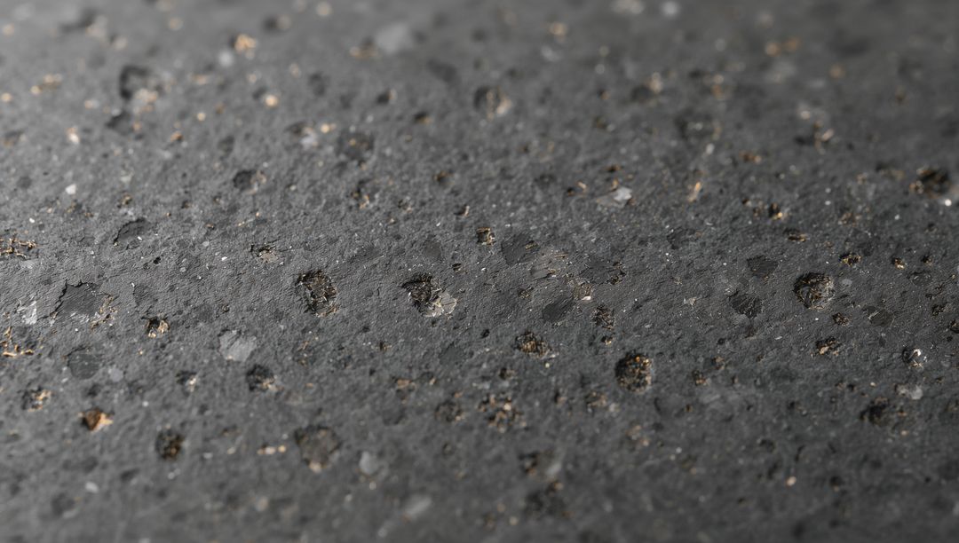 Dark volcanic rock surface showing porous circular pits and mineral fleck macro texture