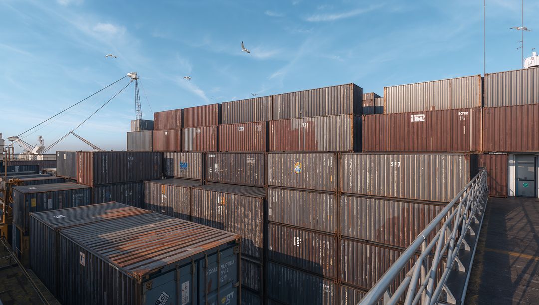 Stacked Rusting Shipping Containers Crowding Port Walkway with Crane and Seagulls