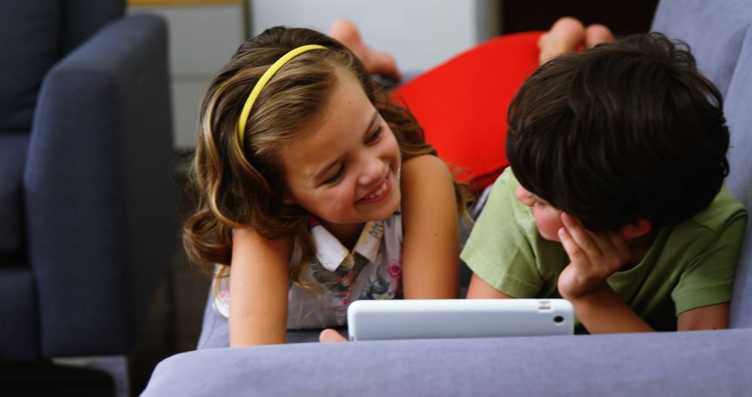 Children Smiling and Watching Tablet on Couch at Home - Free Images, Stock Photos and Pictures on Pikwizard.com