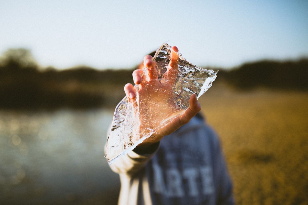 Person Holding Clear Ice on Spring Day Near Riverbank - Free Images, Stock Photos and Pictures on Pikwizard.com