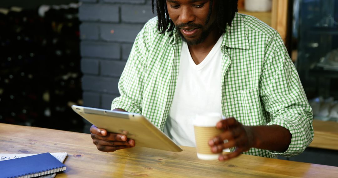 Man enjoying coffee while working on tablet in cozy cafe - Free Images, Stock Photos and Pictures on Pikwizard.com