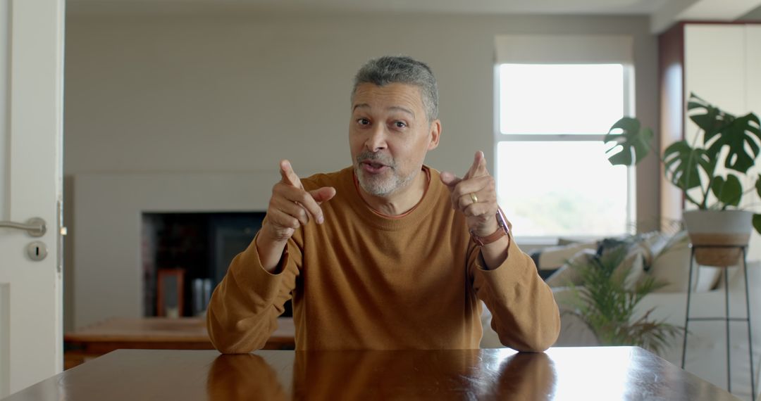 Senior Man Gesturing Enthusiastically at Table in Cozy Room
