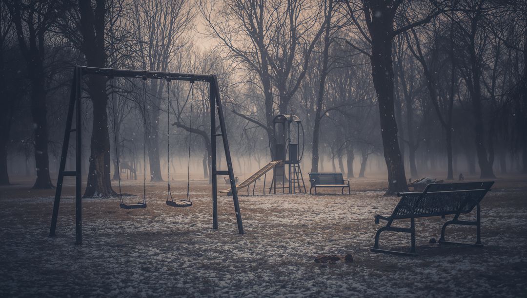 Desolate foggy playground with empty swings and benches in wintry park landscape