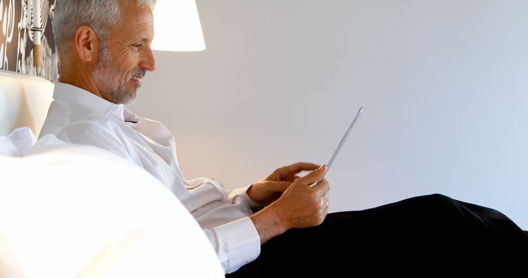 Mature Businessman Relaxing in Hotel Room Using Digital Tablet