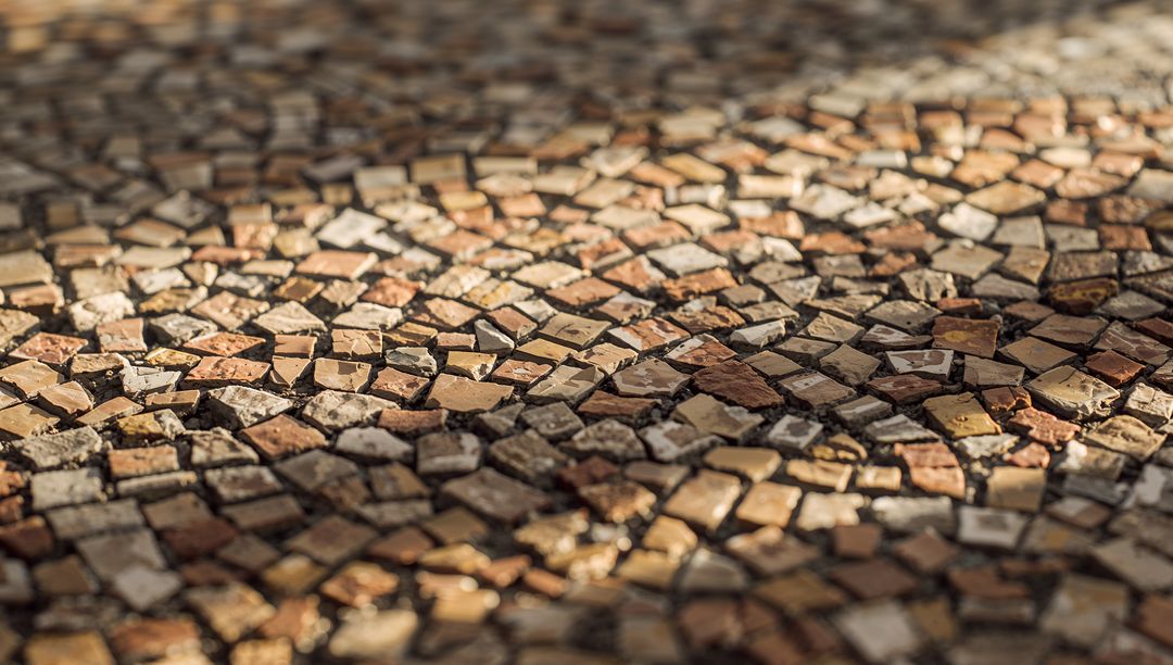 Sunlit mosaic cobblestone pavement showcasing warm tesserae, earthy tones and textured grout
