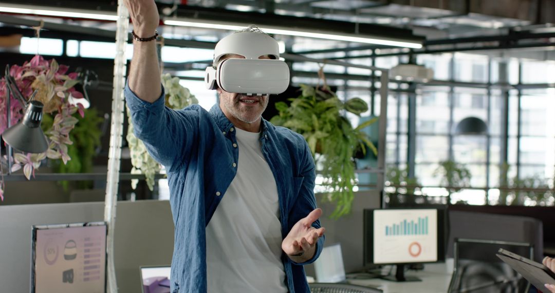 Mature man wearing VR headset interacting in modern open-plan office with data monitors