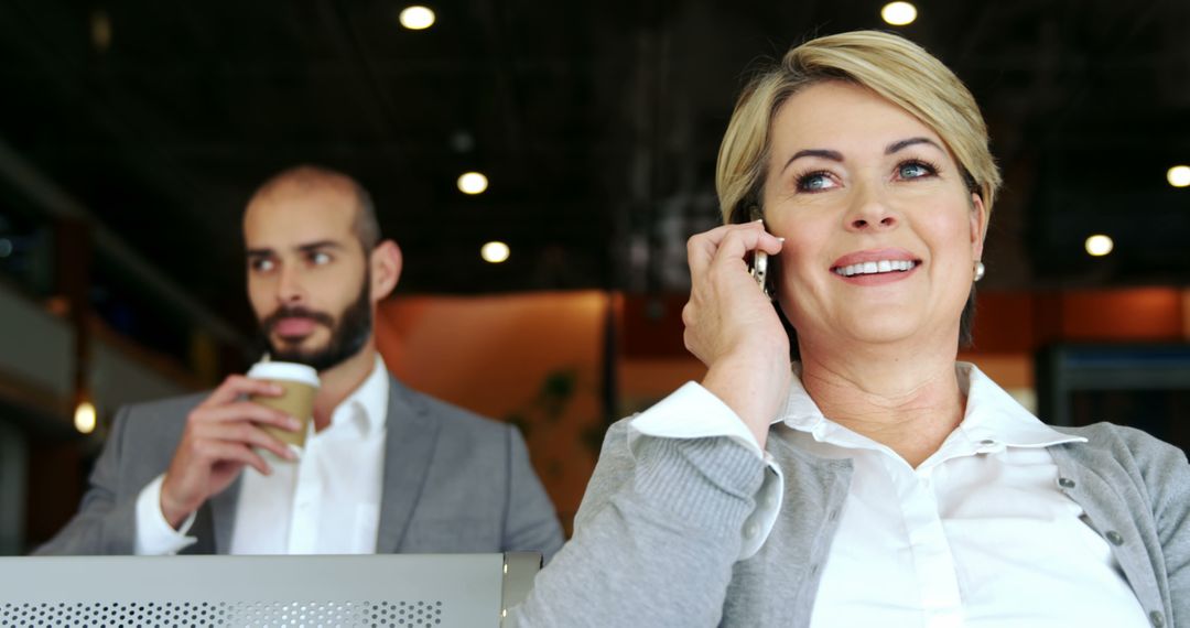 Businesswoman talking on phone while colleague holding coffee in office - Free Images, Stock Photos and Pictures on Pikwizard.com