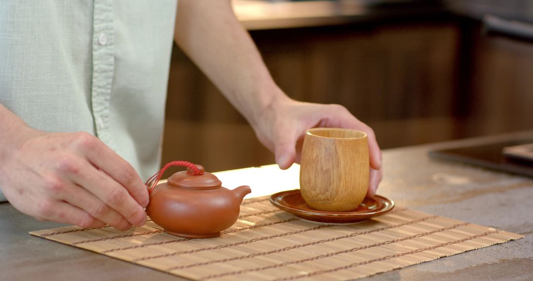 Man Arranging Clay Teapot and Wooden Cup in Rustic Kitchen