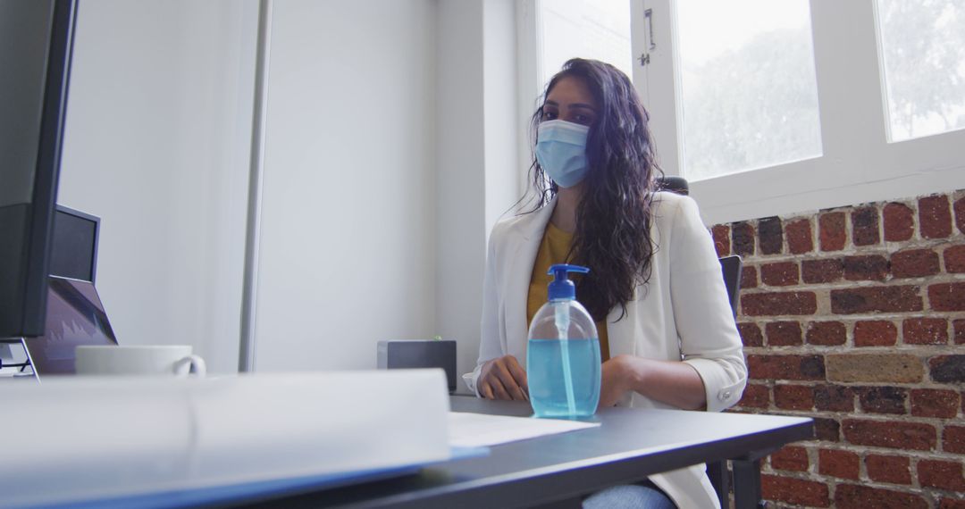 Businesswoman Wearing Mask at Office Desk with Hand Sanitizer - Free Images, Stock Photos and Pictures on Pikwizard.com