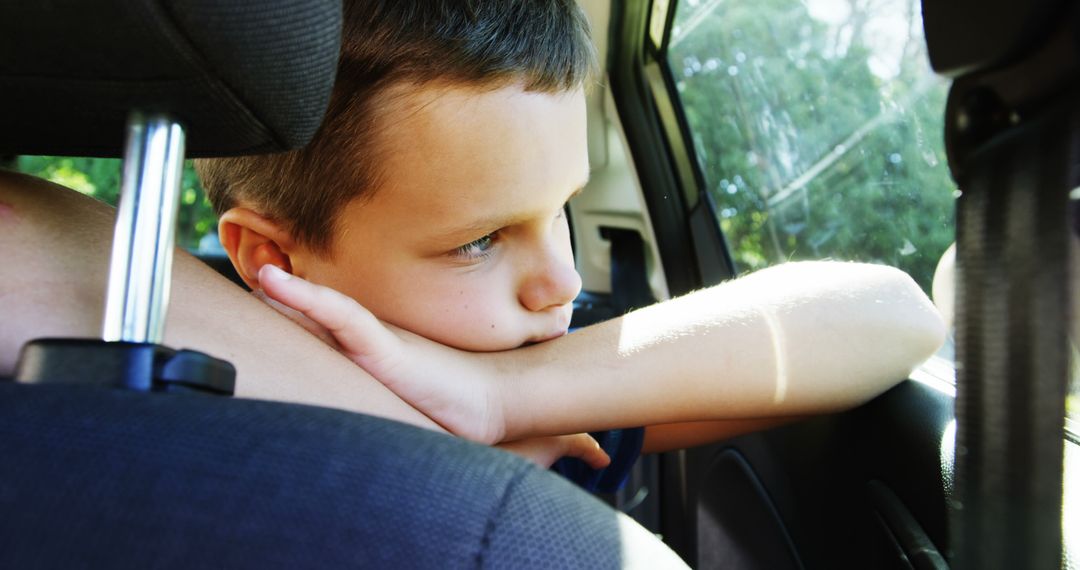 A young Caucasian boy looks out of a car window, resting his chin on his arm, with copy space - Free Images, Stock Photos and Pictures on Pikwizard.com