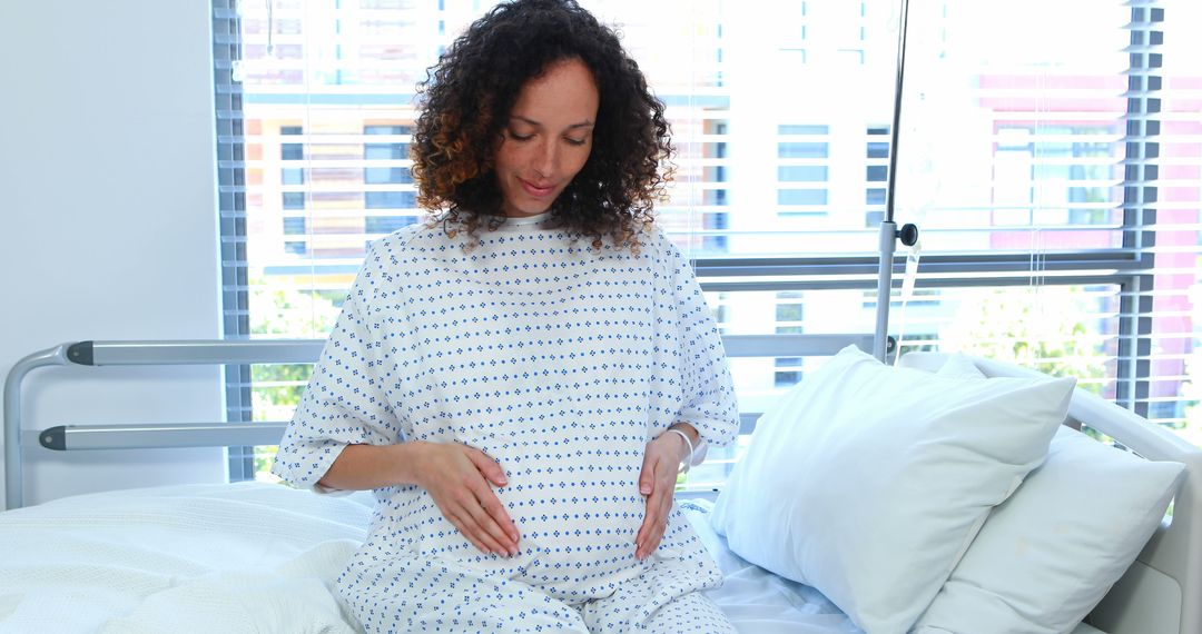 Pregnant woman in hospital gown sitting in hospital bed with hands on belly - Free Images, Stock Photos and Pictures on Pikwizard.com