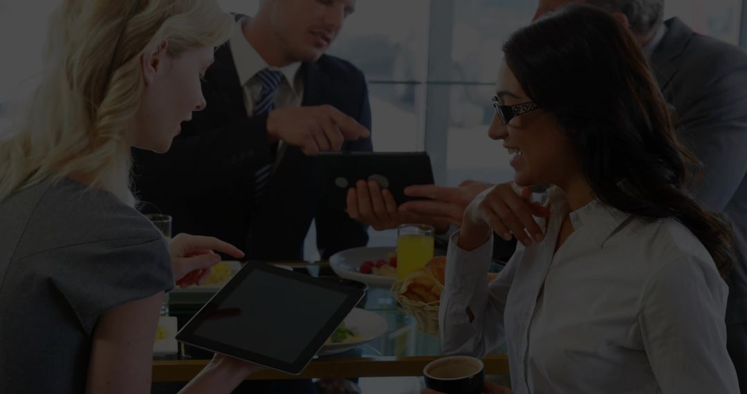 Business team having breakfast meeting with tablets, coffee, fruit in modern daylight office