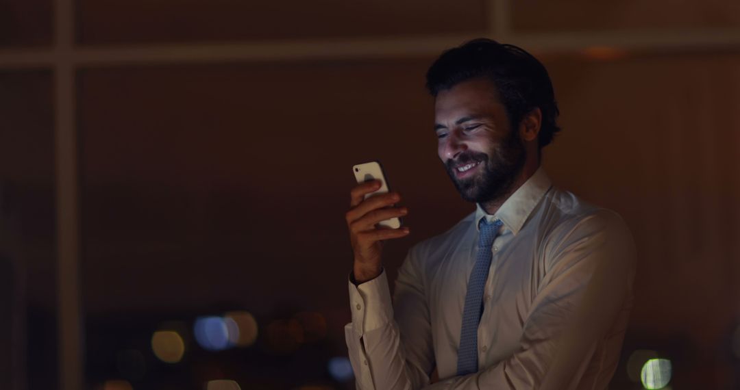 Businessman Smiling at Smartphone Late Night Office - Free Images, Stock Photos and Pictures on Pikwizard.com