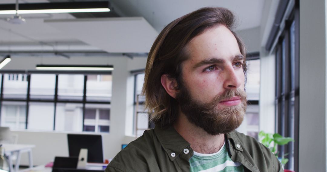 Thoughtful Young Man with Beard in Modern Office - Free Images, Stock Photos and Pictures on Pikwizard.com