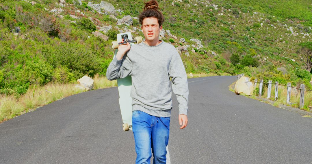 Man Holding Skateboard and Camera Walking on Rural Road - Free Images, Stock Photos and Pictures on Pikwizard.com