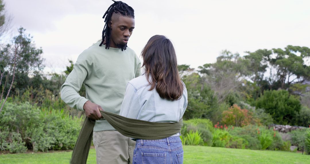 Man wrapping scarf around partner's waist while standing in lush garden showing affection