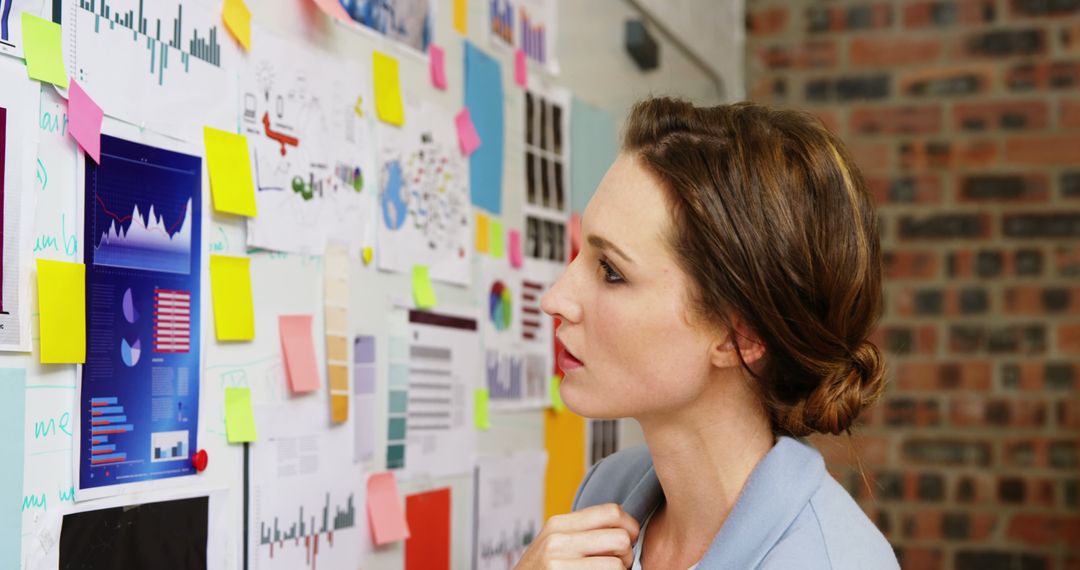 Businesswoman Analyzing Marketing Charts with Sticky Notes on Wall - Free Images, Stock Photos and Pictures on Pikwizard.com