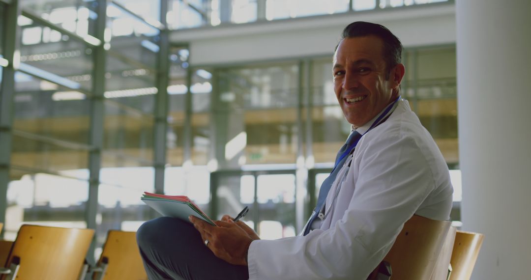 Middle-aged doctor sitting in modern hospital lobby holding clipboard - Free Images, Stock Photos and Pictures on Pikwizard.com