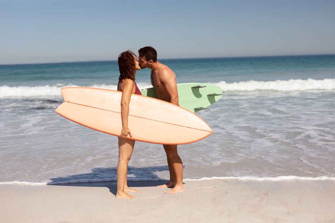Young couple with surfboard kissing each other on beach in the sunshine - Free Images, Stock Photos and Pictures on Pikwizard.com