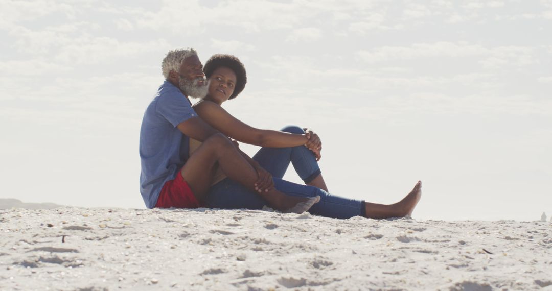 Happy african american couple sitting and embracing on sunny beach - Free Images, Stock Photos and Pictures on Pikwizard.com