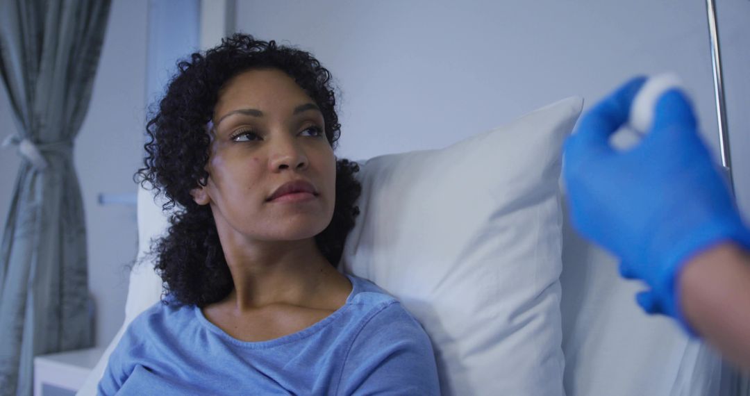 Concerned patient watching gloved nurse preparing injection while resting on hospital bed