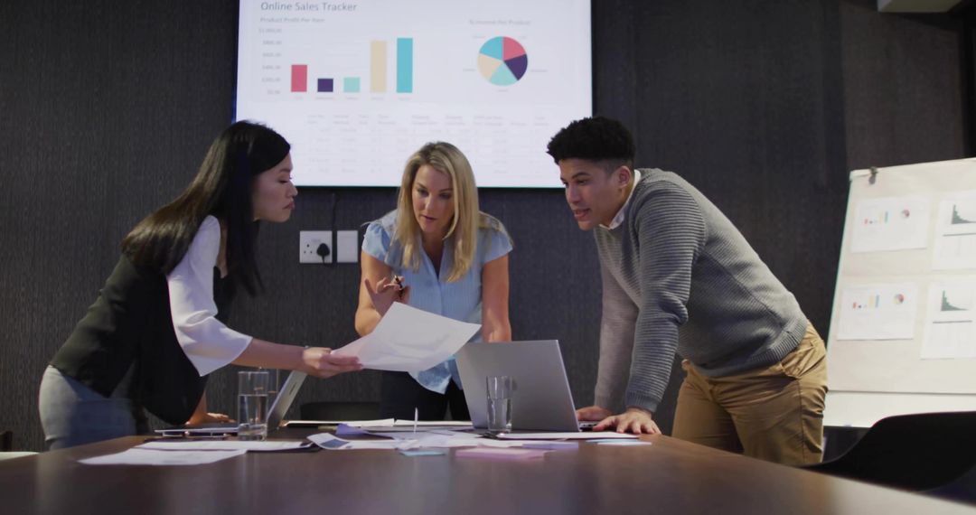 Team collaborating on sales analytics in boardroom with laptop, charts and presentation screen