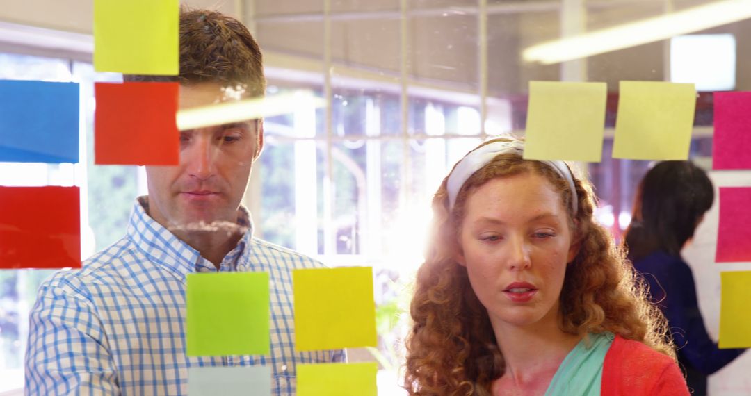 Team Brainstorming with Colorful Sticky Notes on Glass