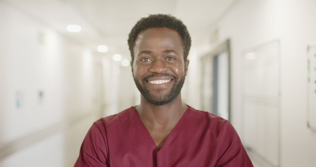 Smiling Healthcare Professional in Red Scrubs Standing in Hospital Corridor - Free Images, Stock Photos and Pictures on Pikwizard.com