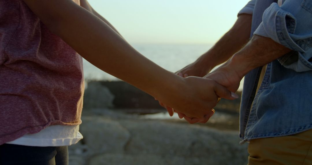 Biracial couple holding hands by sea, showing affection - Free Images, Stock Photos and Pictures on Pikwizard.com