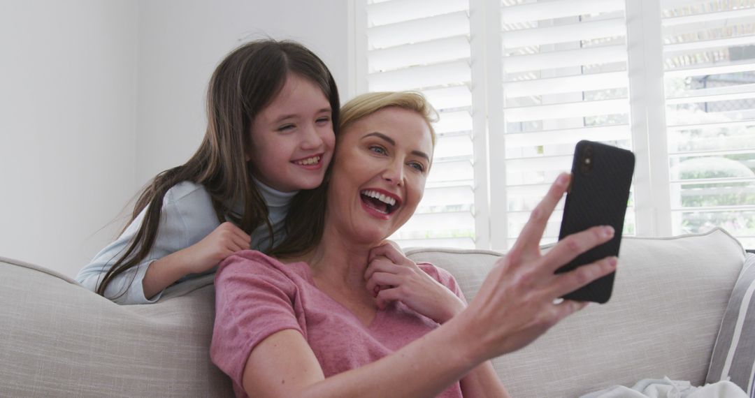 Mother and Daughter Smiling and Taking Selfie Together on Sofa - Free Images, Stock Photos and Pictures on Pikwizard.com