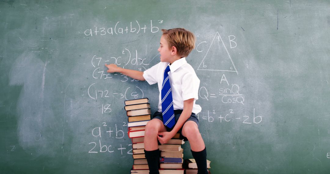 Young Boy Sitting on Books and Studying Math on Chalkboard - Free Images, Stock Photos and Pictures on Pikwizard.com