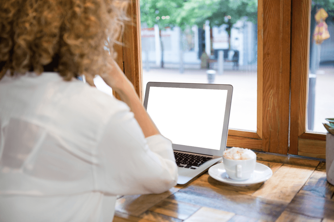 Woman in Cafe Using Laptop with Blank Screen Near Window