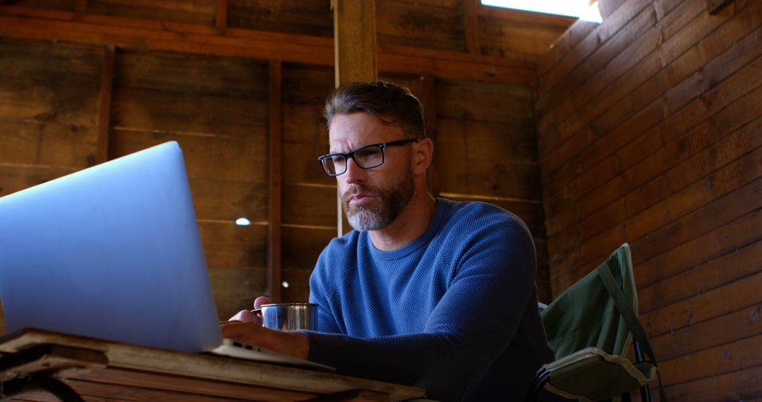 Bearded Man Working on Laptop in Rustic Cabin - Free Images, Stock Photos and Pictures on Pikwizard.com