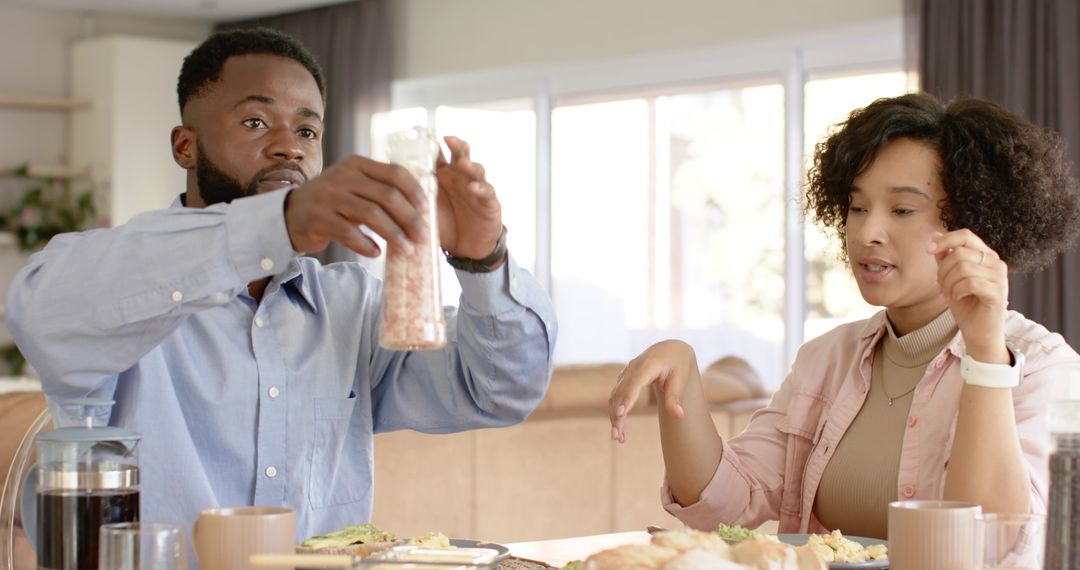 Couple seasoning avocado toast at sunlit breakfast table sharing morning conversation