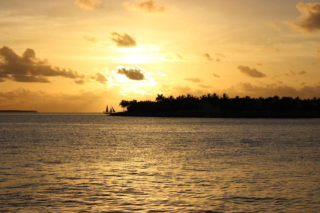 Serene Sunset Over Tropical Shoreline with Silhouetted Boat - Free Images, Stock Photos and Pictures on Pikwizard.com