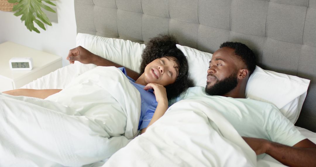 Black couple waking up in bed, woman stretching under white duvet, cozy morning intimacy