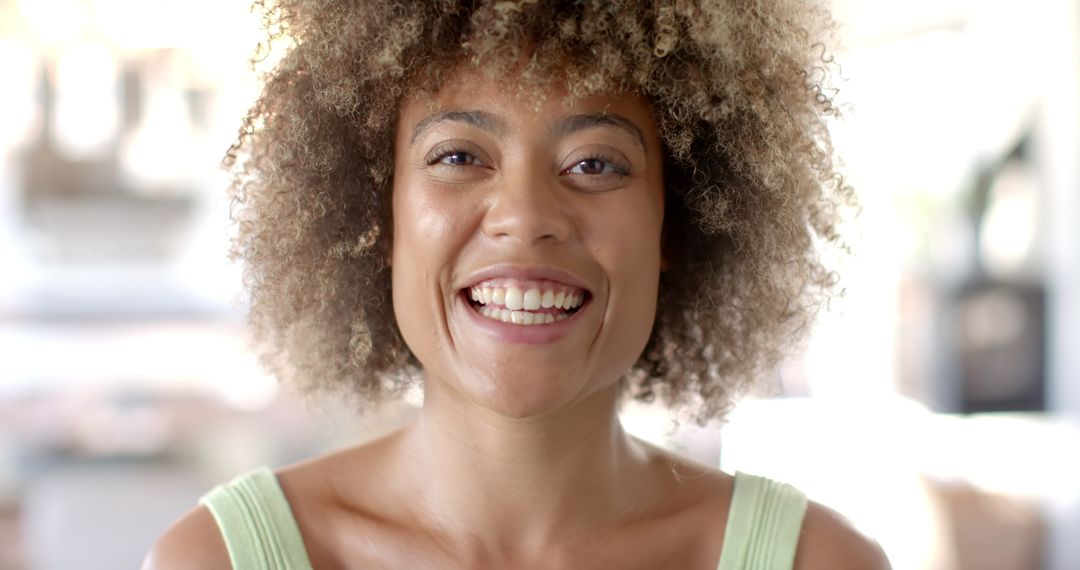 Woman with Curly Hair Smiling in Sunlit Outdoor Scene