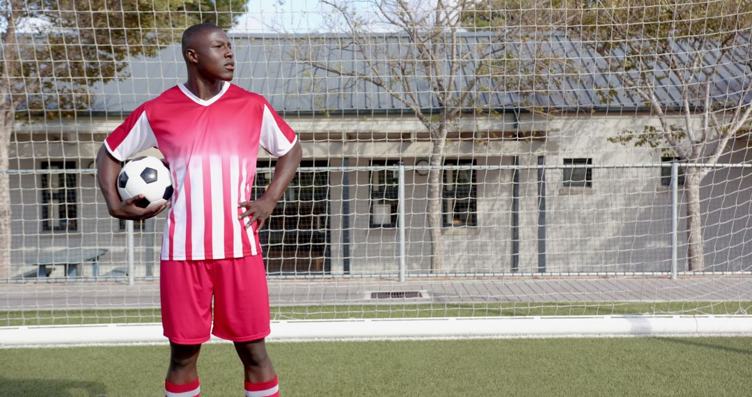 Confident Soccer Player Posing by Goal on Field Holding Ball