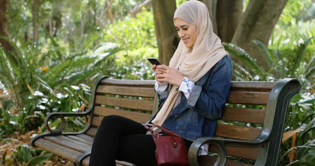 Muslim Woman Relaxing on Park Bench While Using Smartphone - Free Images, Stock Photos and Pictures on Pikwizard.com