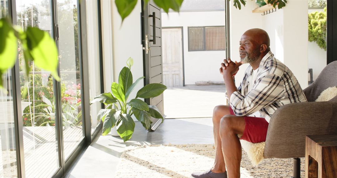 Mature Man Reflecting Peacefully by Large Window at Home