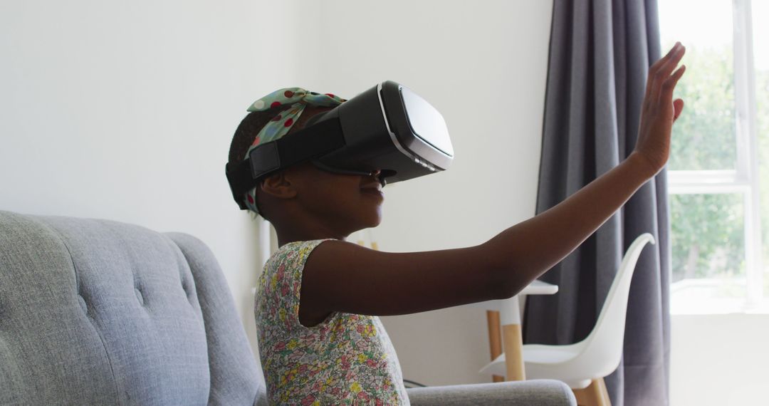 African american girl gesturing while using vr headset sitting on the couch at home - Free Images, Stock Photos and Pictures on Pikwizard.com