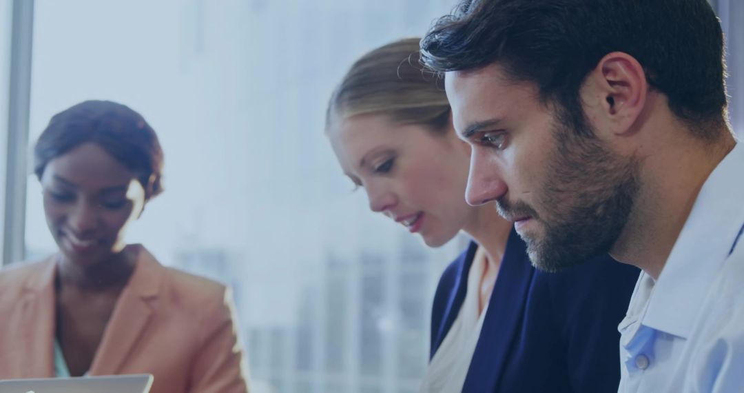 Focused professional collaborating with colleagues around laptop in modern urban office