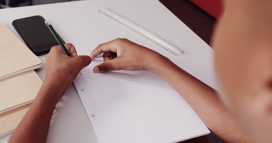 Child Concentrates Writing in Notebook with Pencil at Desk