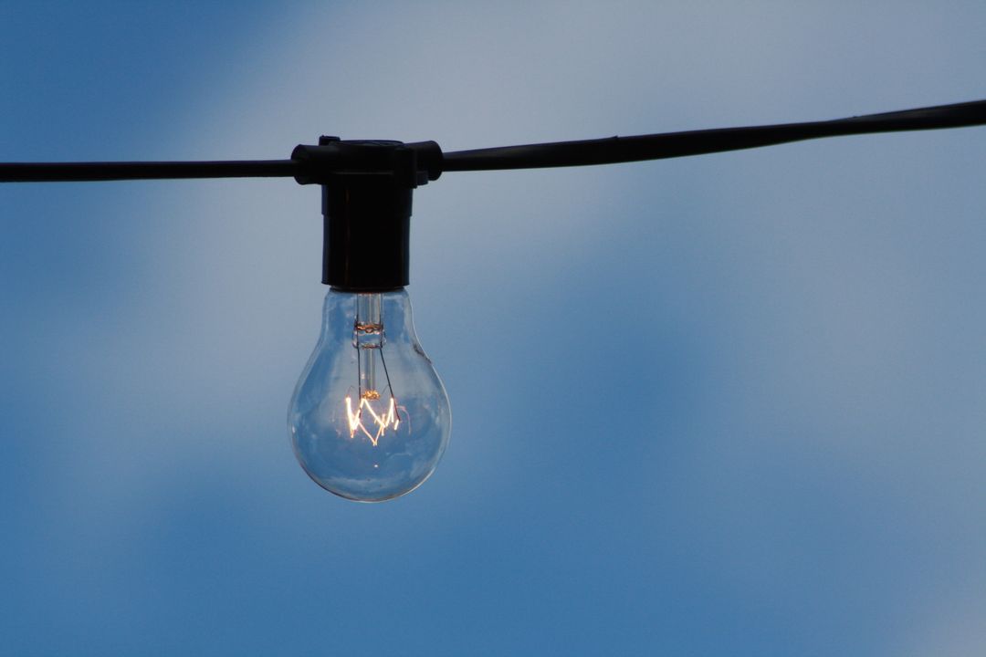 Single Light Bulb Hanging on Wire Against Blue Sky - Free Images, Stock Photos and Pictures on Pikwizard.com