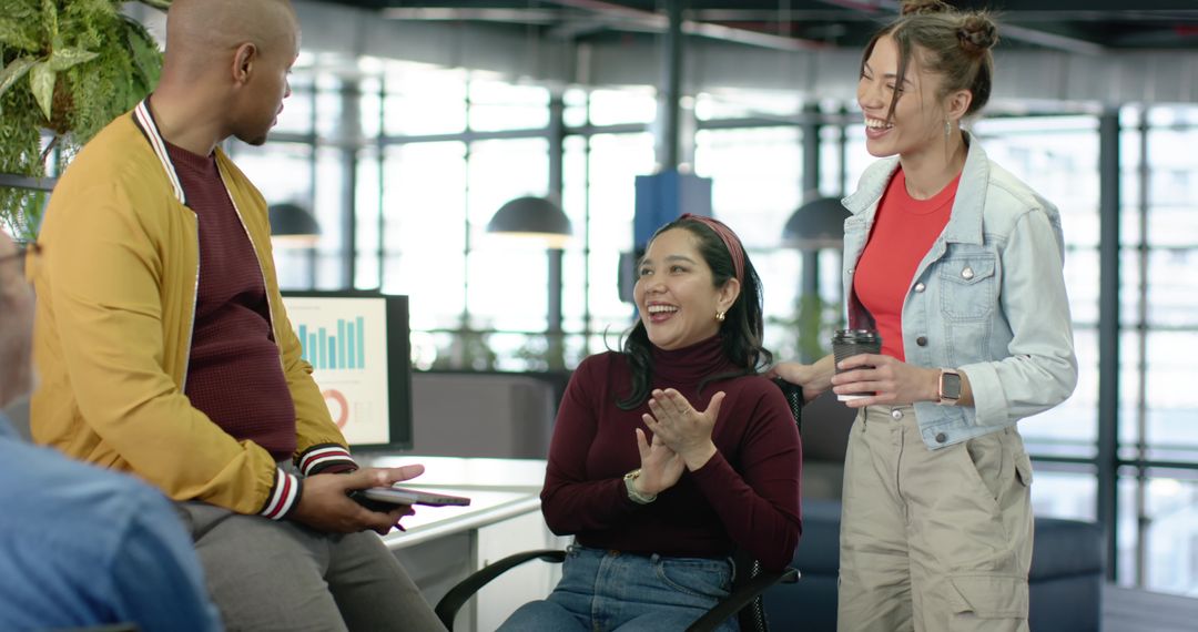 Diverse team celebrating success in modern open-plan office with charts and coffee